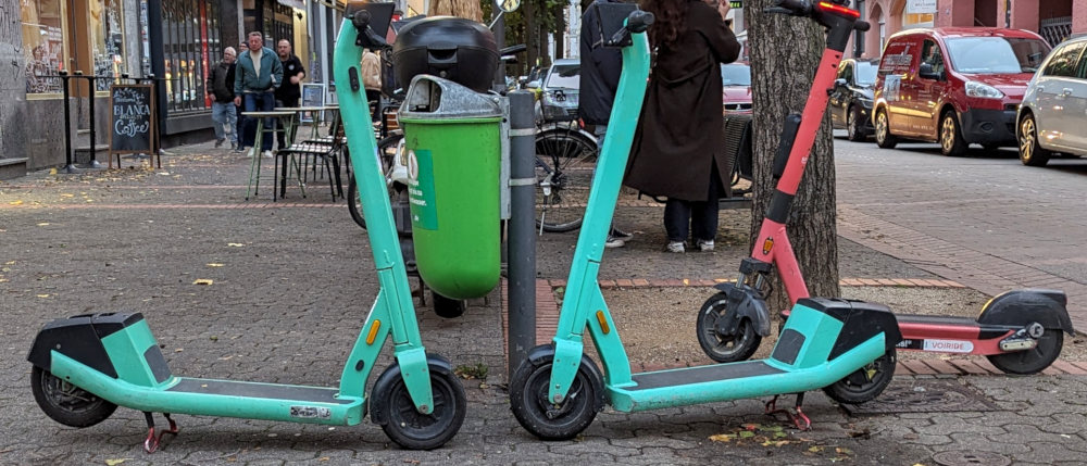 Drei E-Scooter um einen Mülleimer